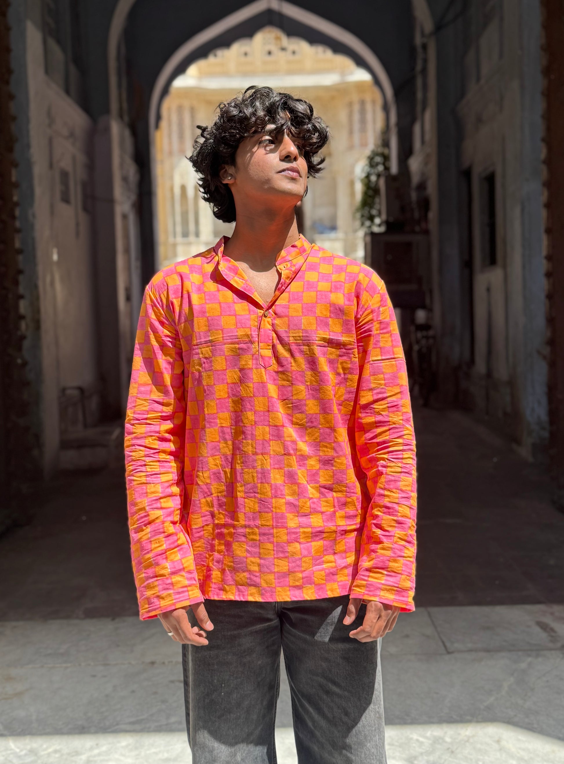 Person wearing a pink and orange checkered shirt standing in an alleyway.