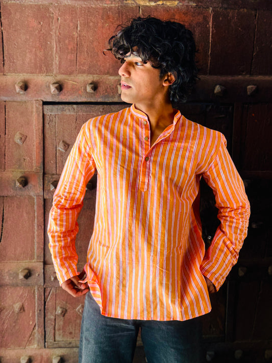 Man wearing an orange and white striped shirt standing against a textured wall.