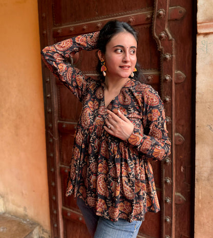 A woman standing with one hand against a door, wearing a black and brown floral kurti with 3/4 length sleeves and a V-neck.