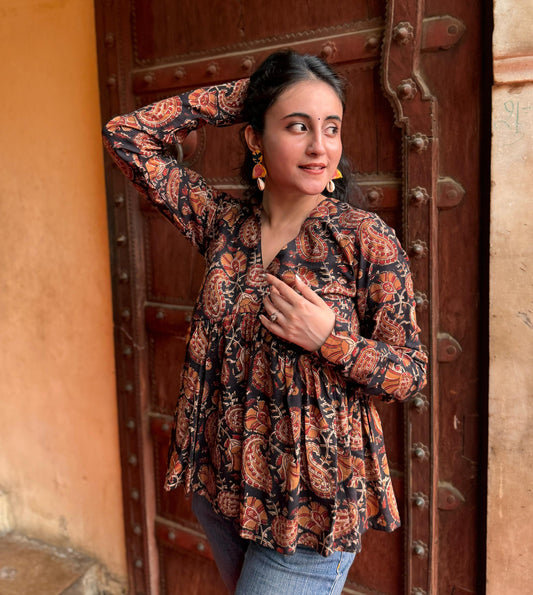A woman standing with one hand against a door, wearing a black and brown floral kurti with 3/4 length sleeves and a V-neck.