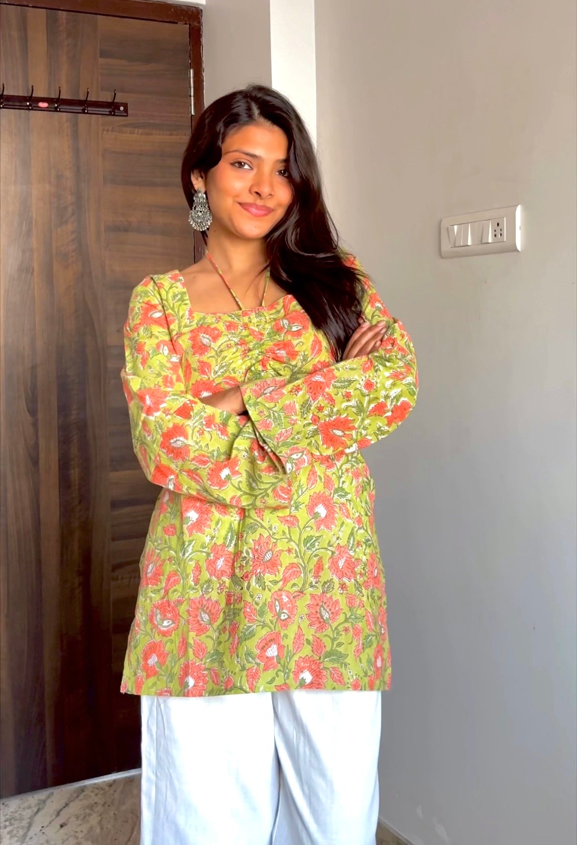 Woman wearing a green floral top and white pants indoors.