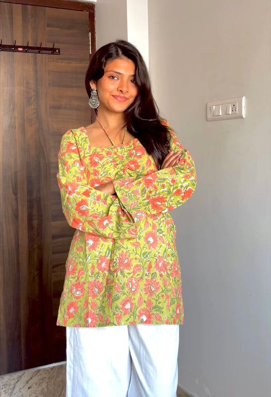 Woman wearing a green floral top and white pants indoors.