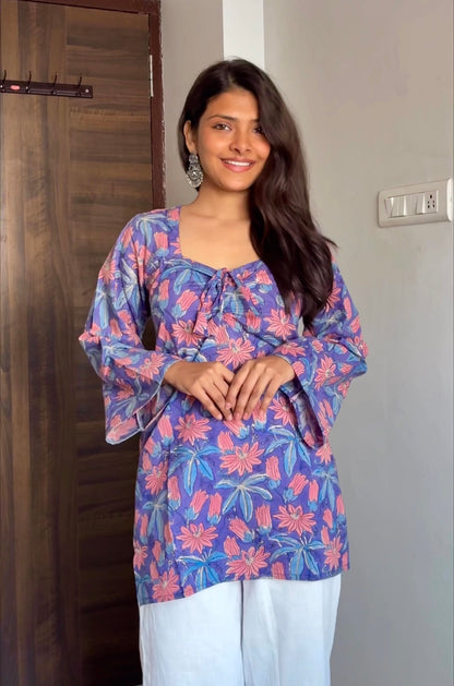 Woman wearing a colorful floral blouse standing indoors.