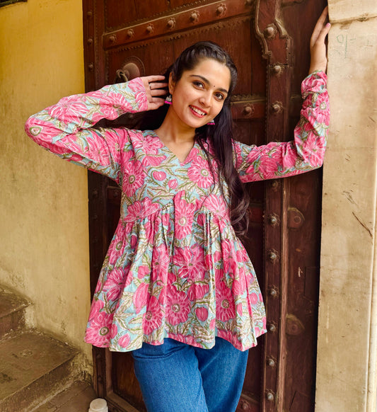 A woman wearing a pink floral hand-block print top with long sleeves and a flared design.