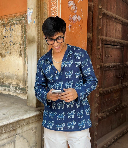 Person wearing a blue patterned shirt standing in front of a textured wall and wooden door.