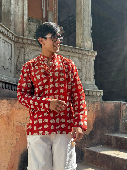 Person wearing a red patterned shirt standing in front of an architectural structure.