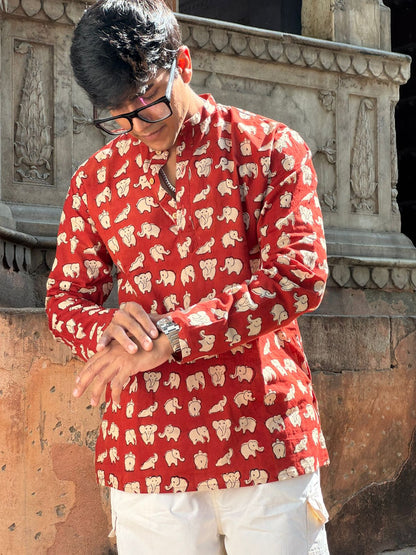 Person wearing a red shirt with white patterns standing in front of stone architecture.