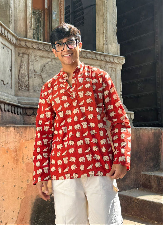 Person wearing a red patterned shirt standing in front of an ornate building.