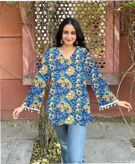 Woman wearing a blue floral blouse with yellow flowers in an outdoor setting.