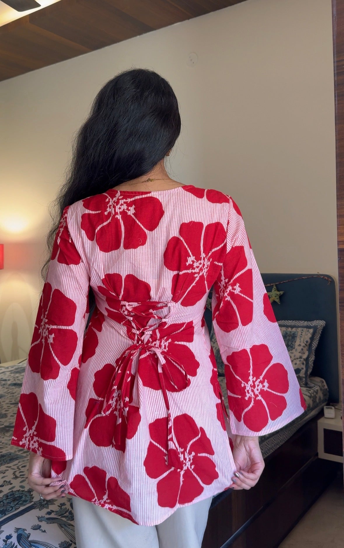 Person wearing a red floral kimono-style garment in a room with a couch and lamp.