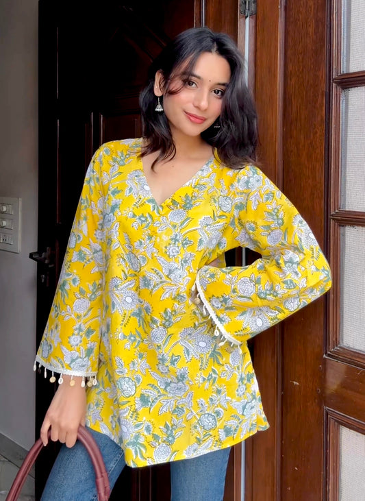 Woman wearing a yellow floral blouse standing in front of a wooden door.