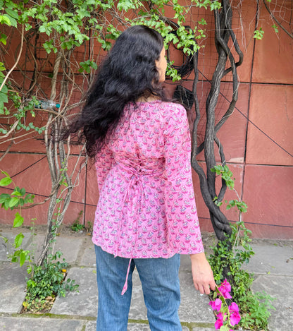 Person wearing a pink floral jacket and blue jeans standing near a red wall with greenery.