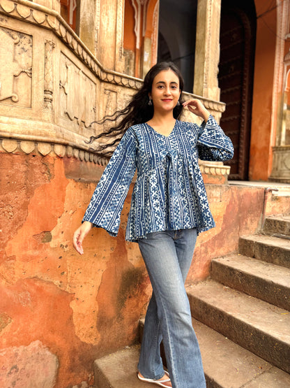 Woman in a blue patterned top and jeans standing on steps with an ornate wall in the background