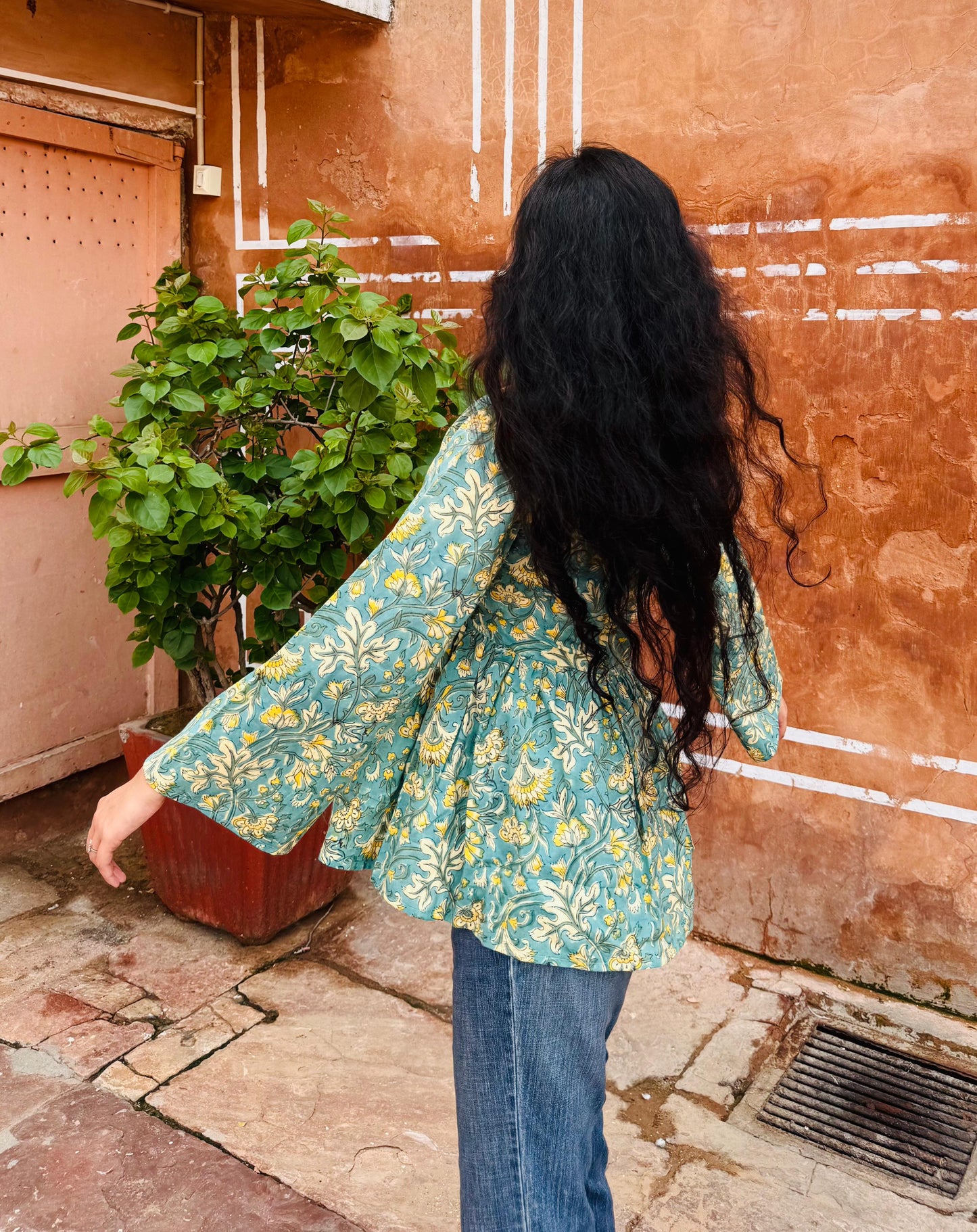 Person wearing a floral jacket and blue jeans standing in front of a textured wall.