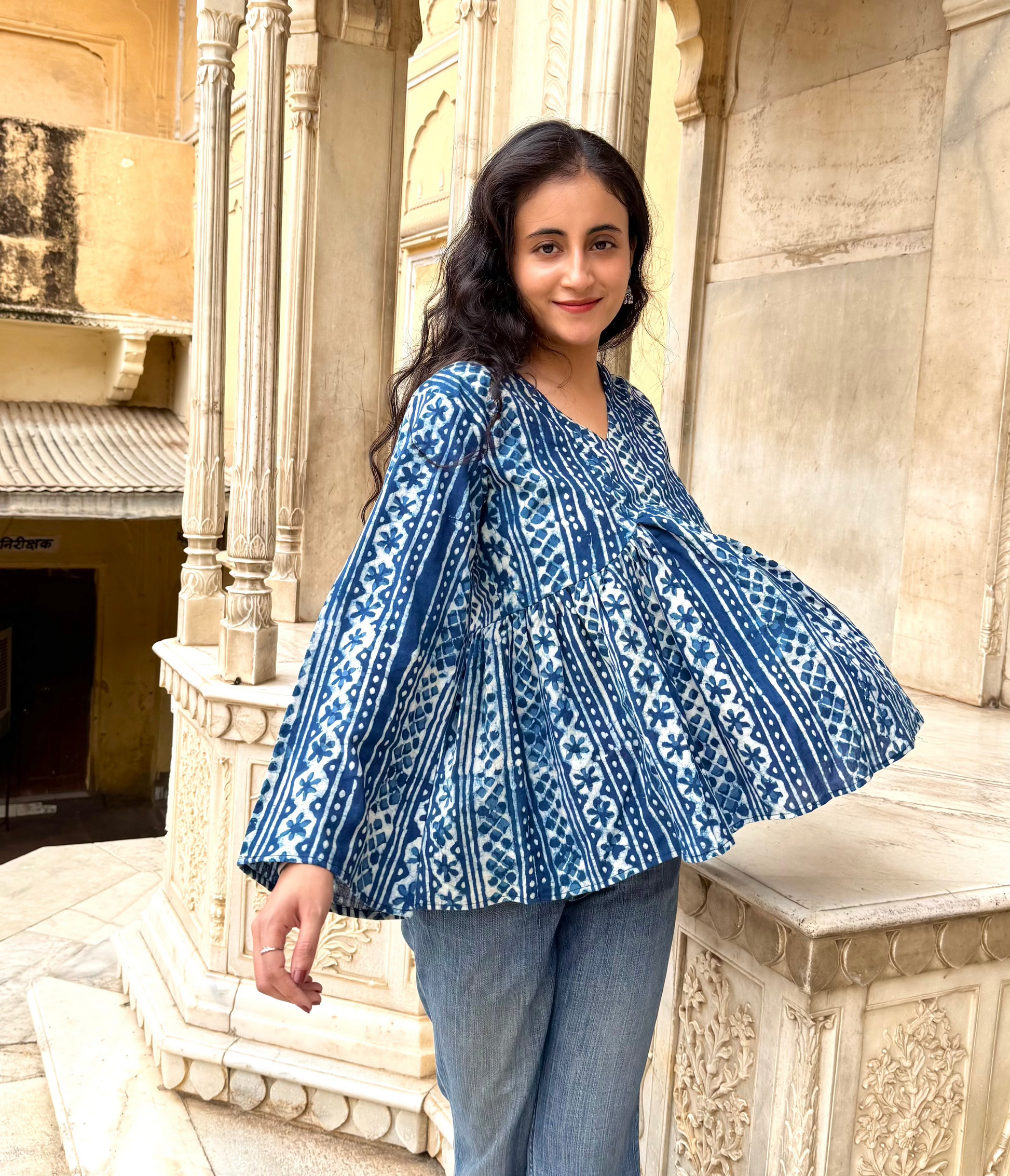 Woman wearing a blue patterned blouse standing in front of stone architecture.