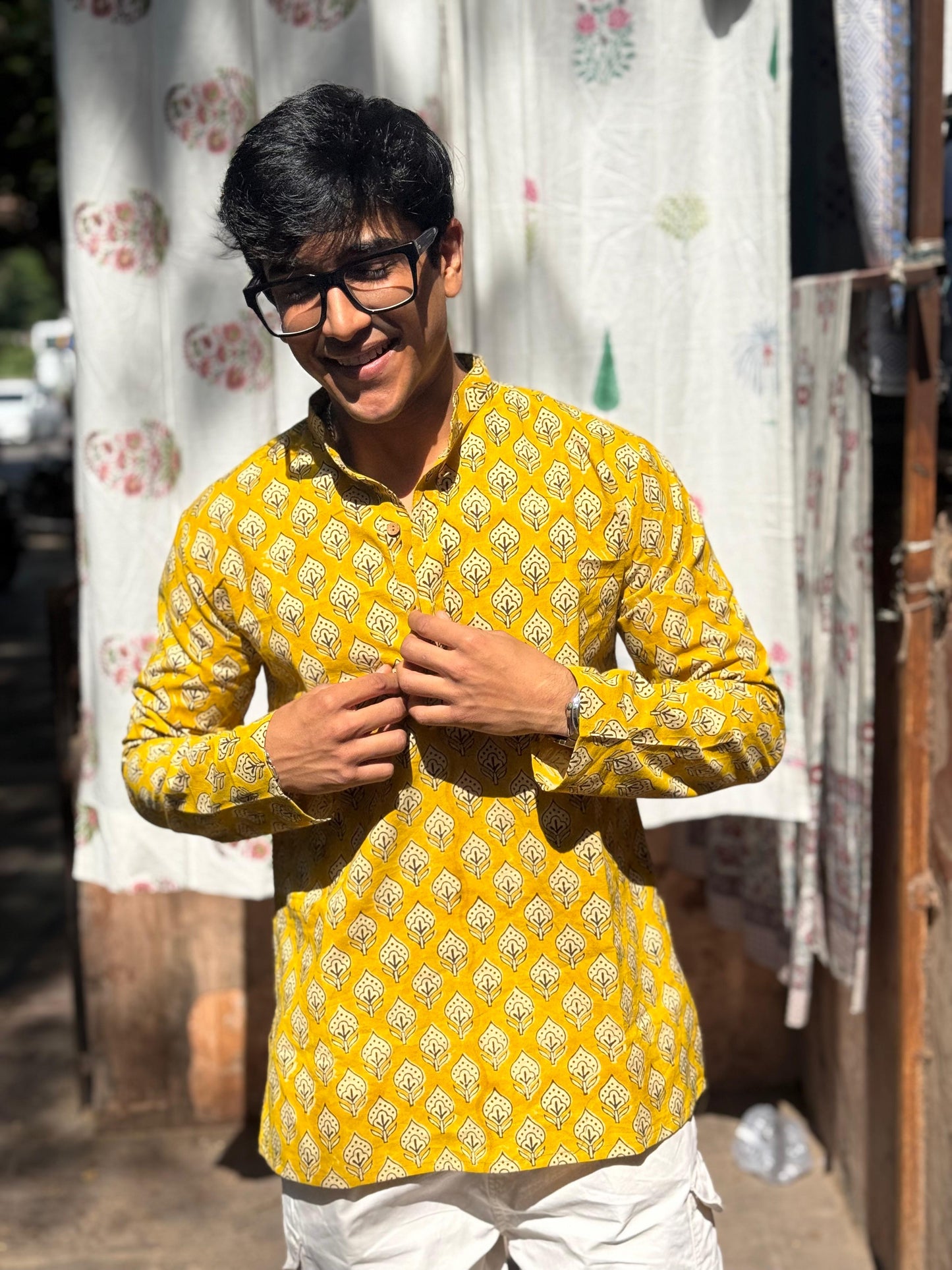 Man wearing a yellow patterned shirt standing in front of a curtain