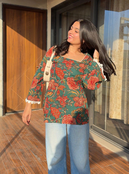 Woman wearing a floral top and jeans standing in a sunlit room.