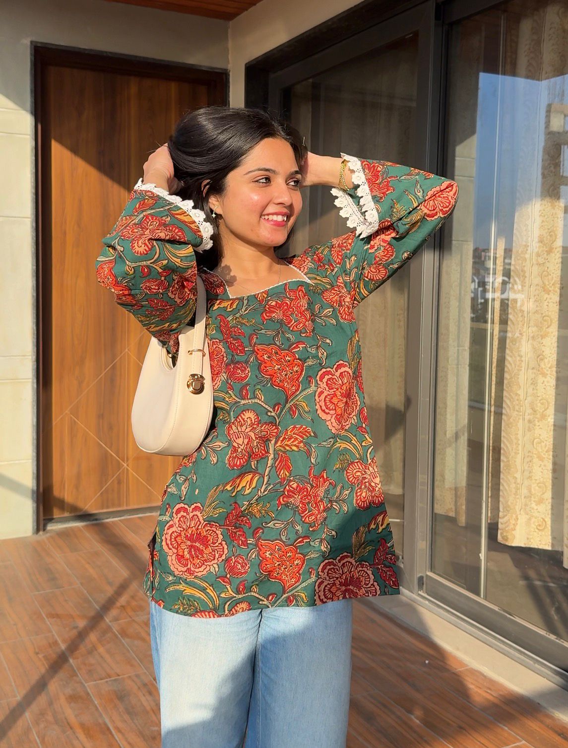 Woman wearing a floral top and jeans, standing in front of a building entrance.