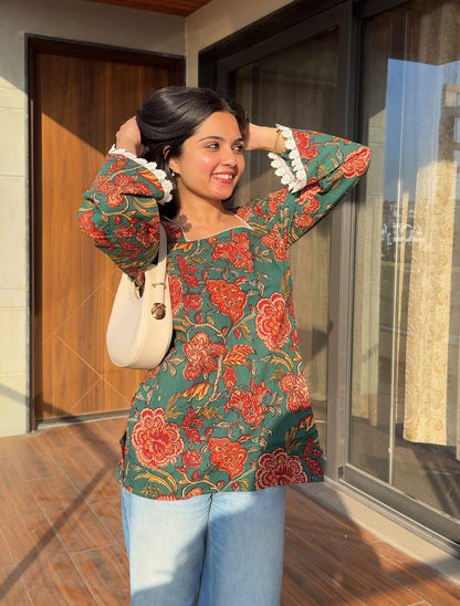 Woman wearing a floral top and jeans, standing in front of a building entrance.