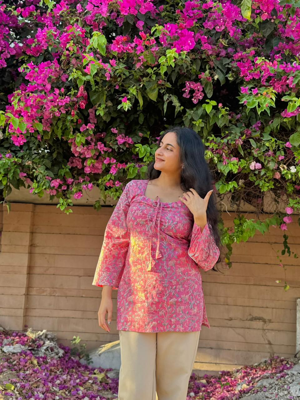 Woman in a pink floral top standing in front of a wall with pink flowers