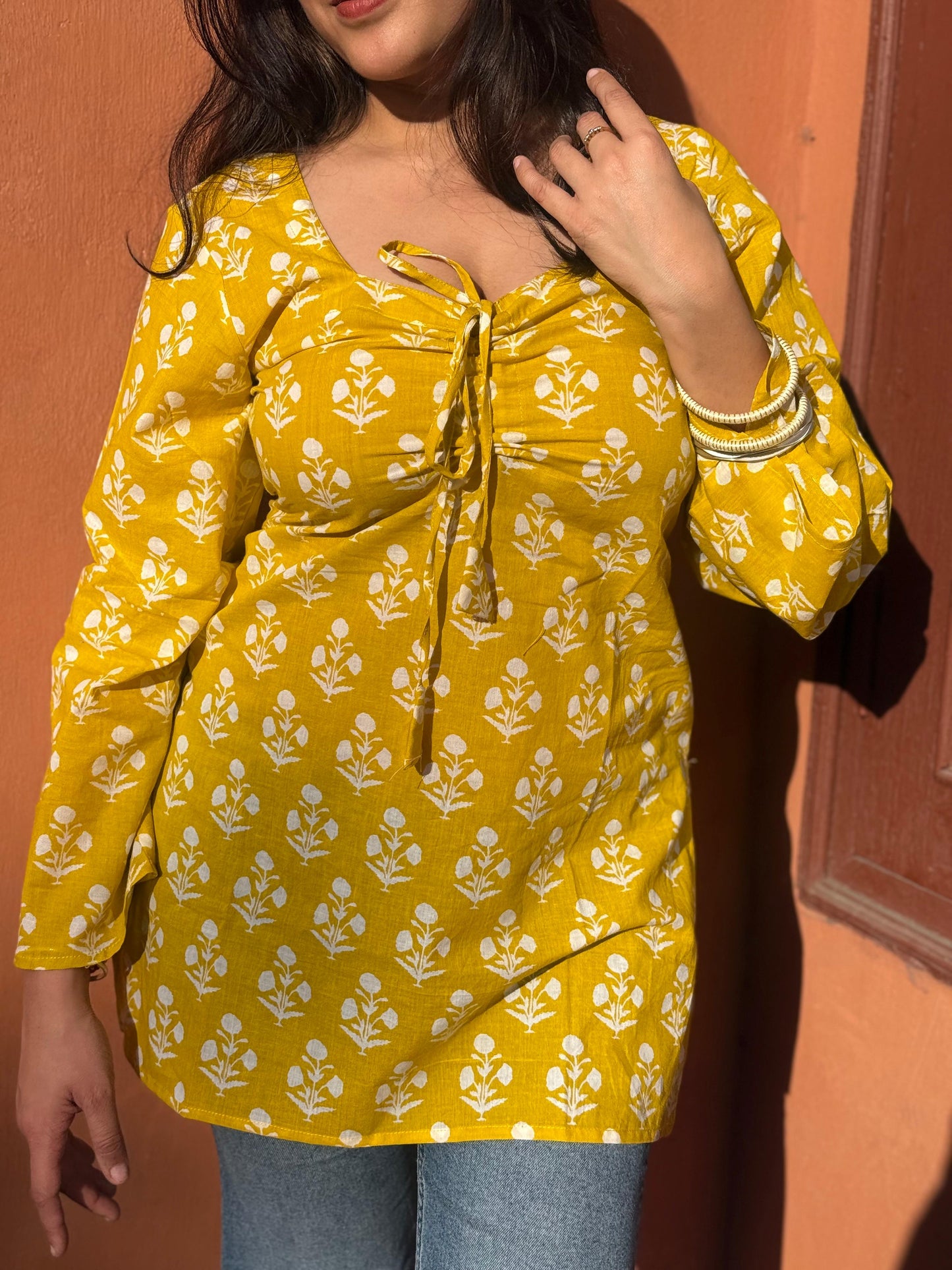 Yellow floral blouse worn by a person against an orange wall