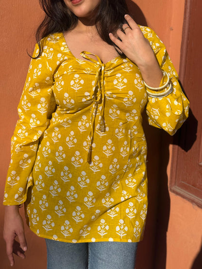 Yellow floral blouse worn by a person against an orange wall