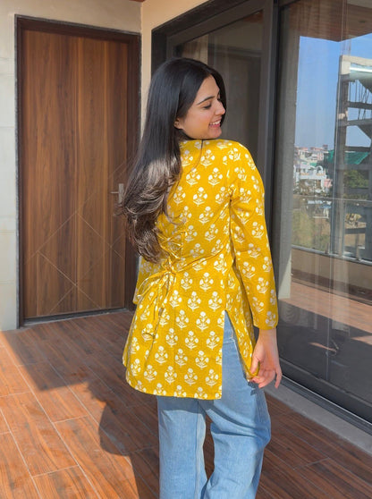 Woman wearing a yellow floral blouse and blue jeans standing on a wooden floor.