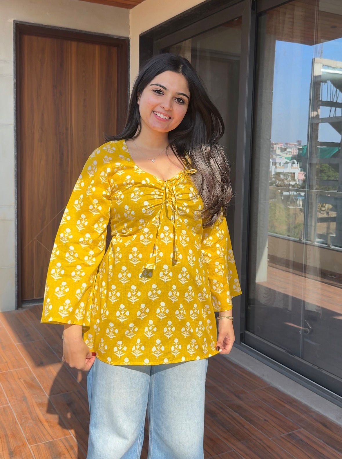 Woman wearing a yellow floral blouse standing indoors.