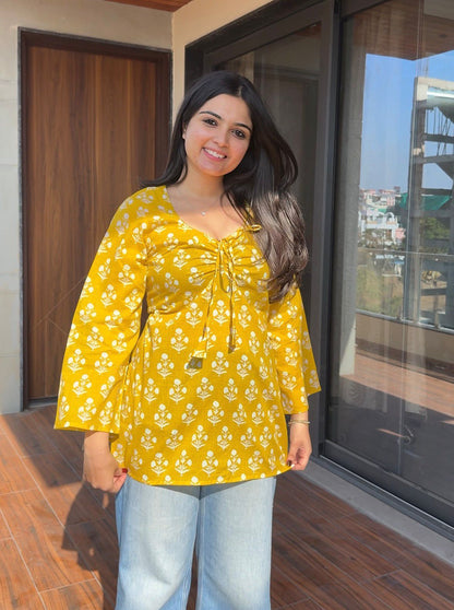 Woman wearing a yellow floral blouse standing indoors.