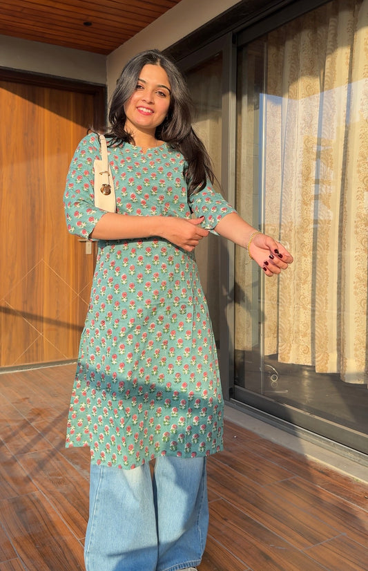 Woman wearing a green floral kurta with blue jeans standing indoors.