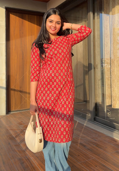 Woman in a red patterned dress standing outdoors with a wooden door in the background