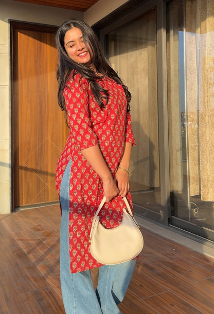 Woman in a red patterned dress holding a beige handbag on a wooden floor.
