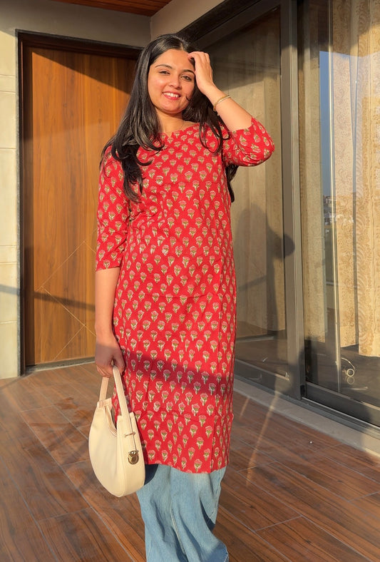 Woman in a red patterned dress standing on a wooden floor.