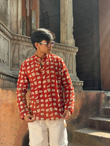 Person wearing a red patterned shirt standing in front of an architectural structure.