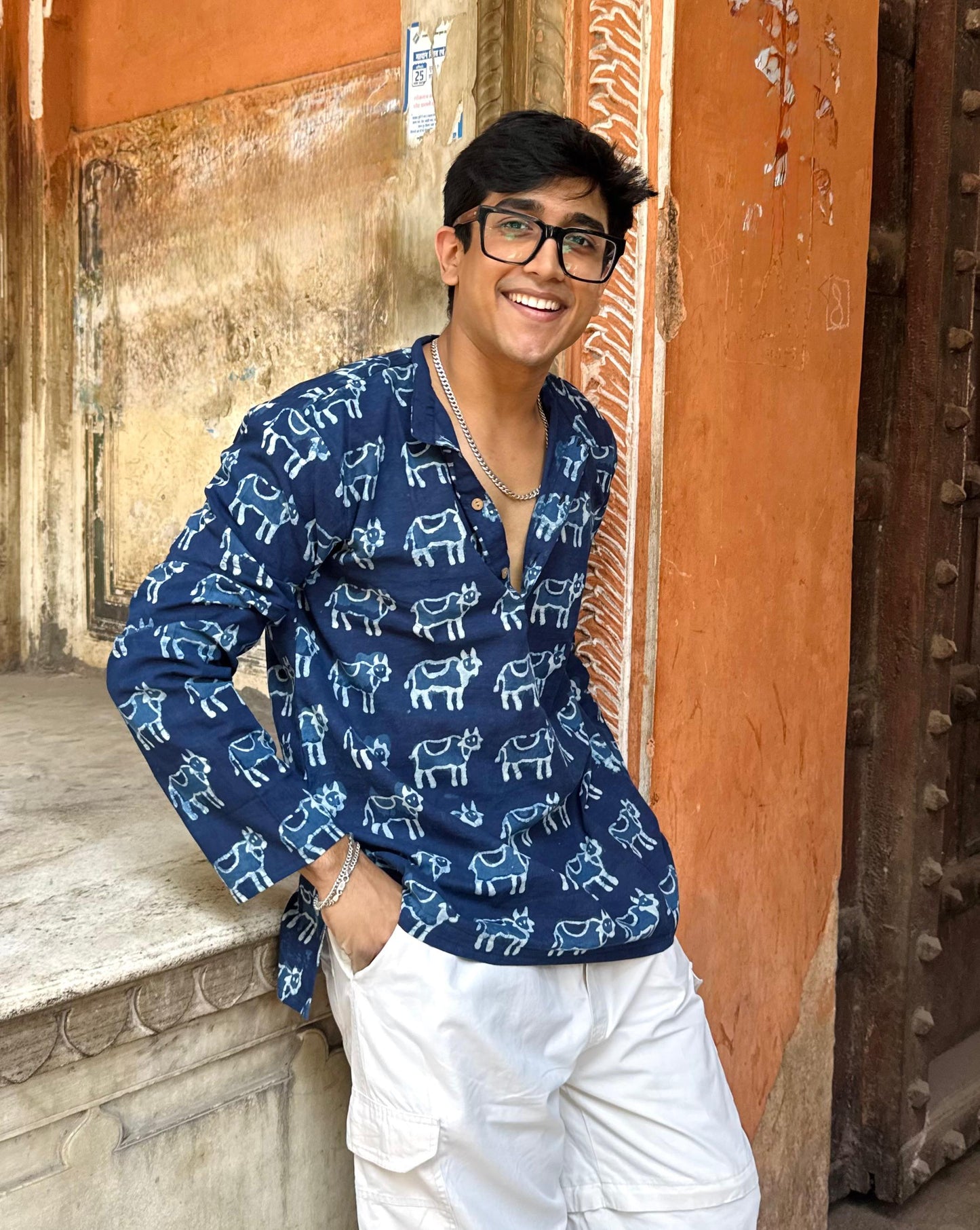 Person wearing a blue patterned shirt standing in front of an ornate door.