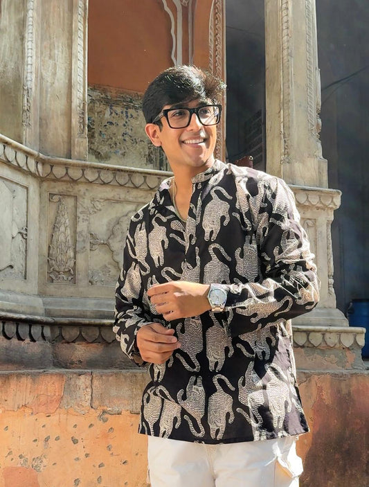 Man wearing a patterned shirt and glasses standing in front of an architectural structure.