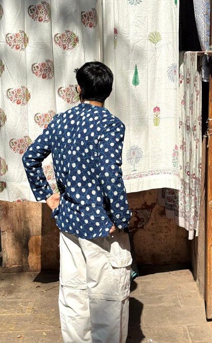 Person wearing a blue polka dot shirt standing in front of patterned curtains.