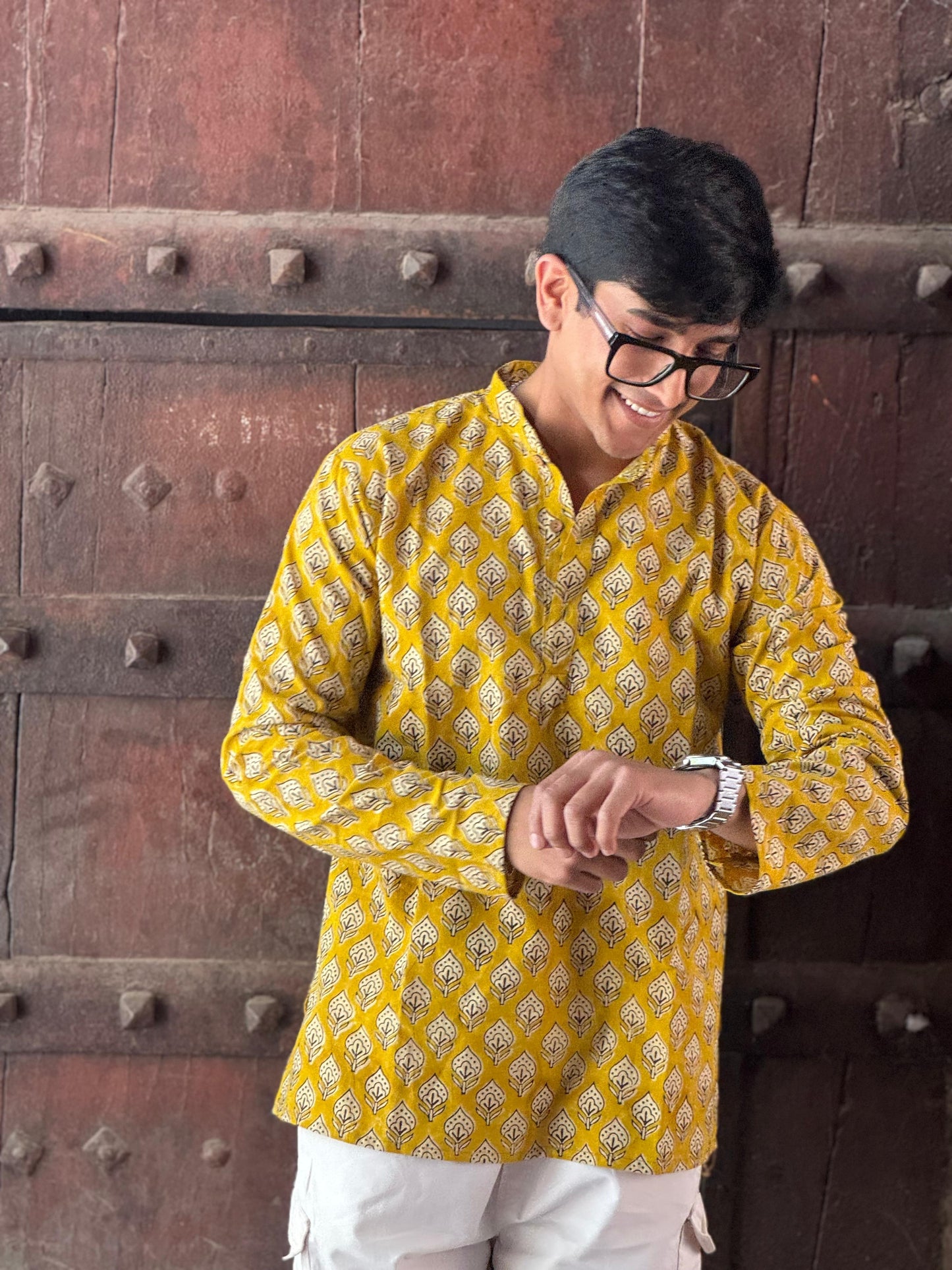 Man wearing a yellow patterned kurta standing in front of a wooden door.