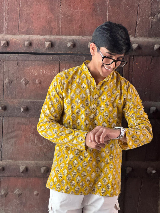 Man wearing a yellow patterned kurta standing in front of a wooden door.