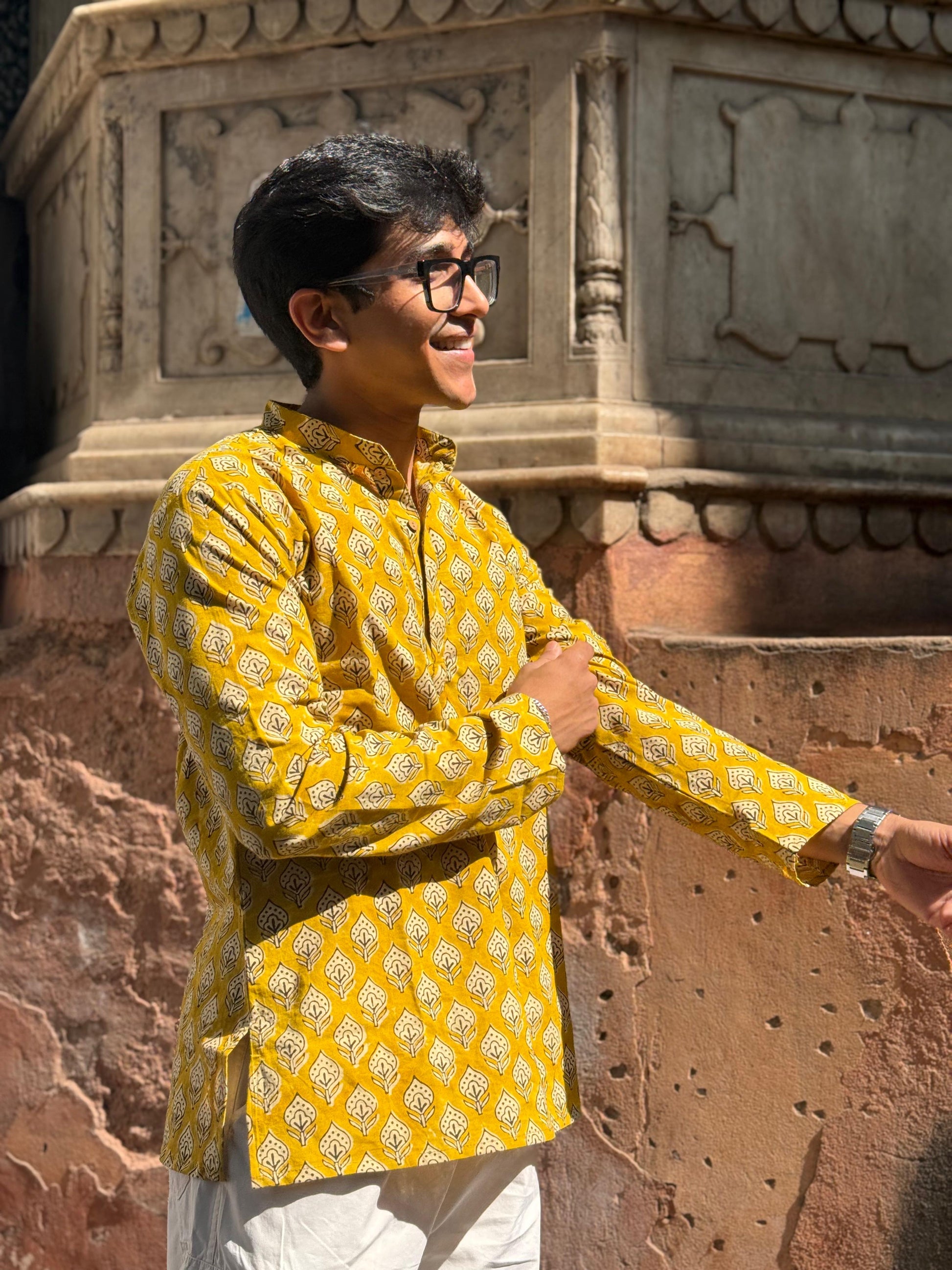Person wearing a yellow patterned kurta standing against an architectural background