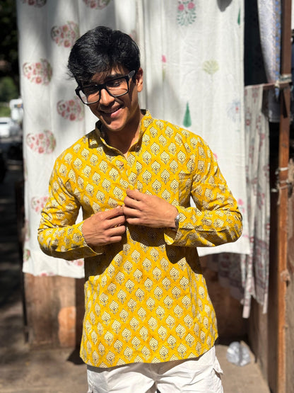 Man wearing a yellow patterned shirt standing in front of a curtain