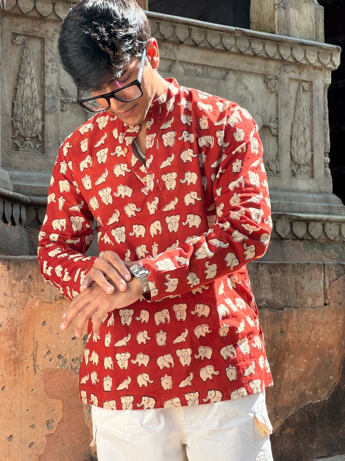 Person wearing a red shirt with white patterns standing in front of stone architecture.