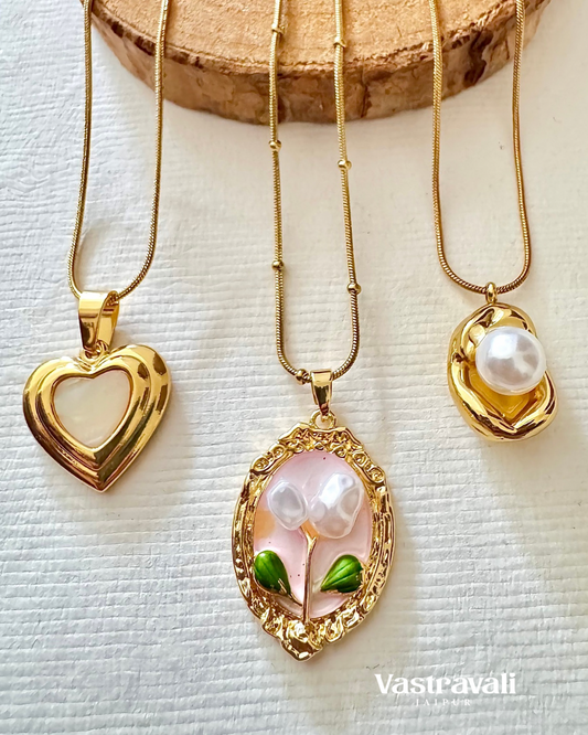 Three gold necklaces with pendants on a textured white surface, featuring the brand 'Vastravali'.