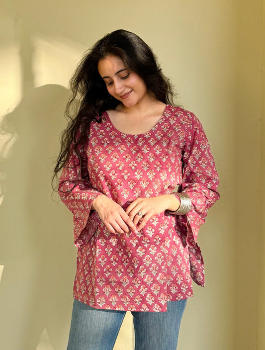 A woman wearing a pink hand-block printed short kurti with flared sleeves, paired with blue jeans.