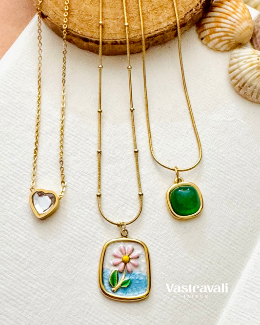 Three gold necklaces with different pendants on a white surface with seashells.